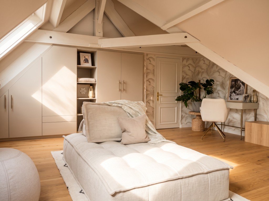 Comble aménagé : banquette, rangements intégrés beige, bureau et lumière zénithale, tons crème et bois clair.