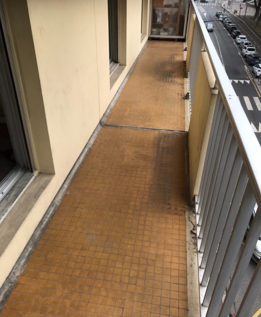 Balcon long et étroit, carrelage terne et rangements visibles, sans aménagement d'accueil.