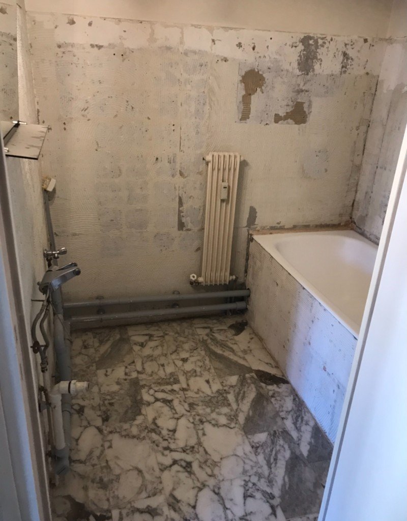 Salle de bain avant travaux : murs décapés, tuyauteries visibles et baignoire non finie.