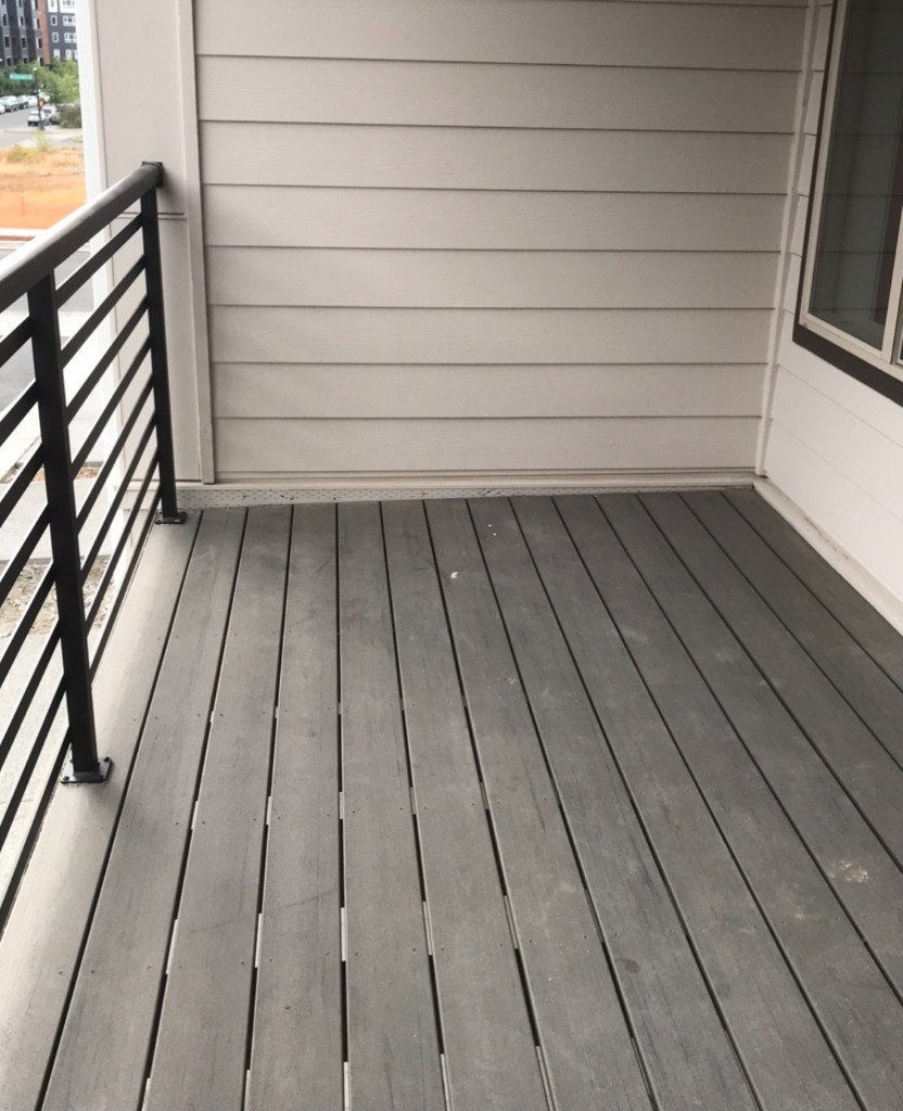 Balcon vide : carrelage gris, garde-corps métallique et murs clairs, sans aménagement d'accueil.