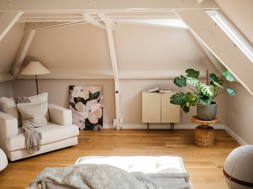 Combles après aménagement : fauteuil, plantes, poufs et décoration chaleureuse sous la charpente blanche.
