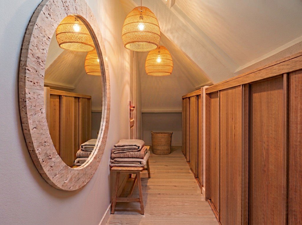 Dressing en enfilade après transformation : color drenching beige, rangements sur-mesure, miroir rond et suspensions en rotin.