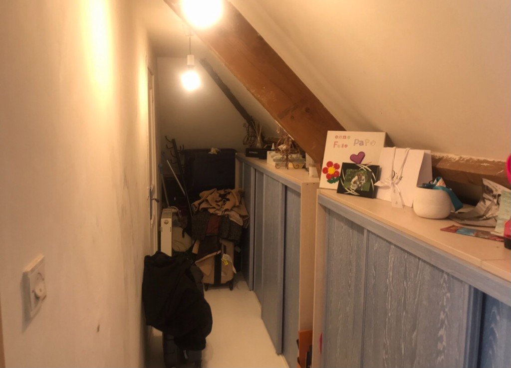 Dressing en enfilade avant réaménagement : zone de stockage sous combles, rangements encombrés et éclairage sommaire.