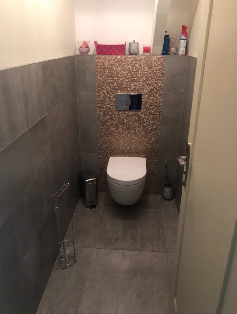 Petite pièce technique avant réorganisation : carrelage gris, WC suspendu et rebord encombré sous combles.