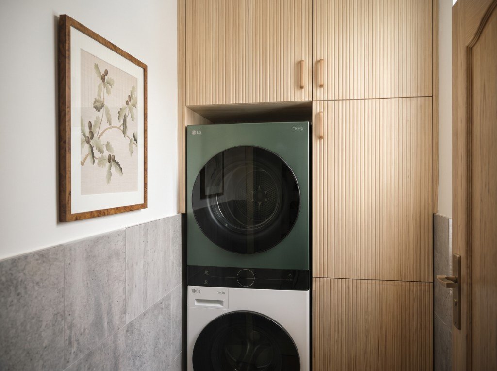 Buanderie après travaux : meubles en bois cannelé, lave-linge et sèche-linge intégrés, affiche botanique au mur.