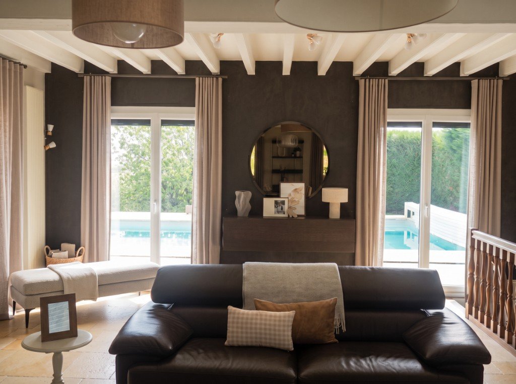 Mur TV après transformation : fond brun profond, miroir rond, console en noyer et rideaux sur mesure.